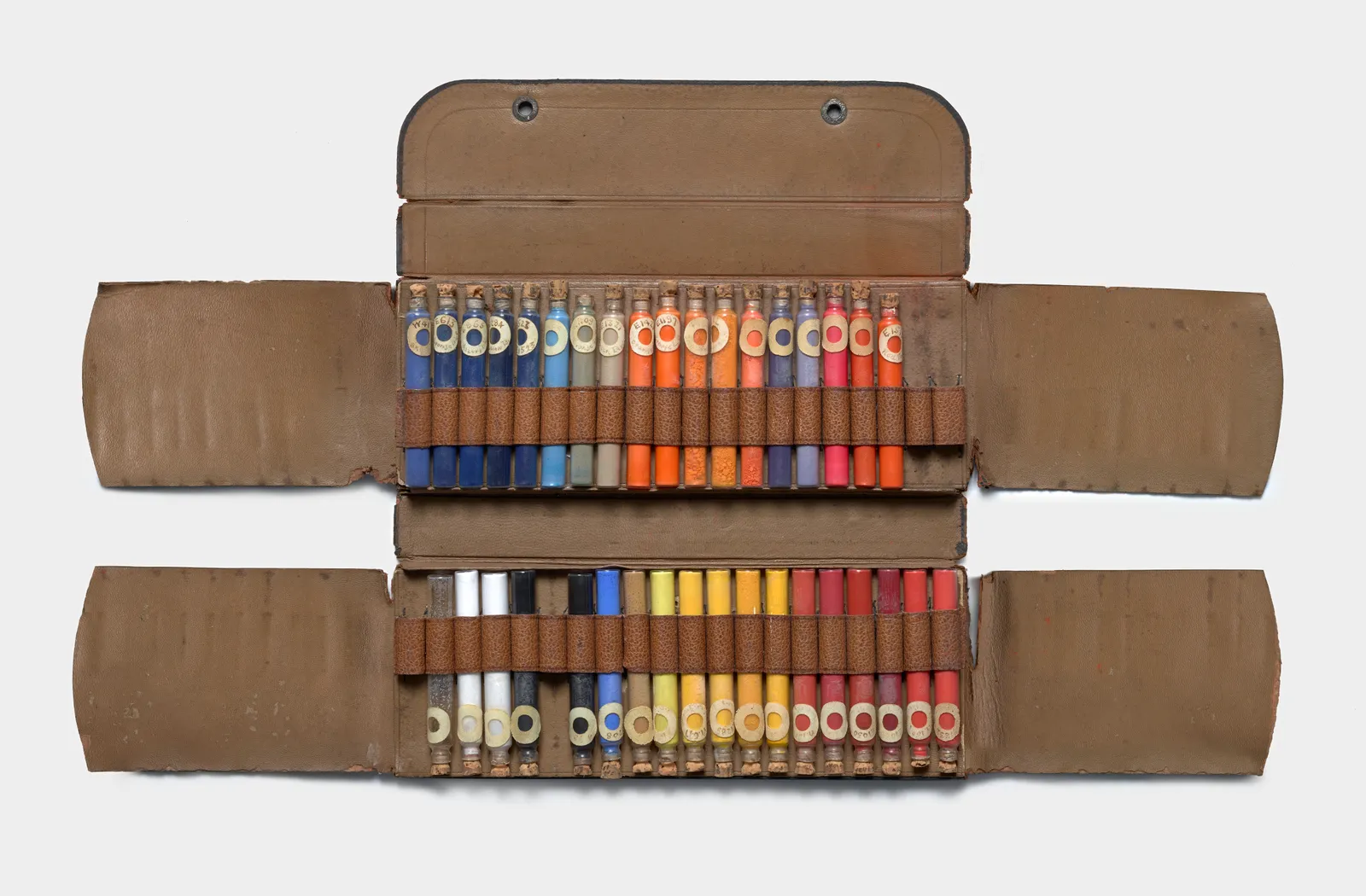 Coffret d'atelier en cuir ouvert, garni de deux rangées de fioles de pigments en poudre : bleus, ocres, rouges, blancs et noirs.